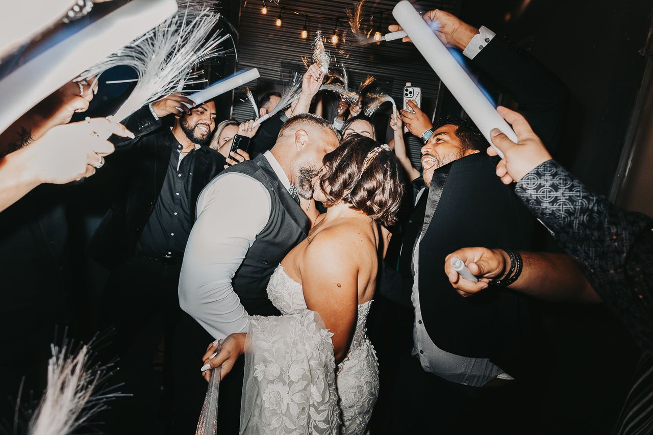 People celebrate and dance energetically at a wedding reception with hands raised in the air while enjoying the festivities.