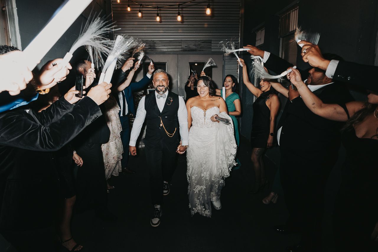Wedding couple walks through a corridor lined with guests holding sparklers during their grand exit celebration.