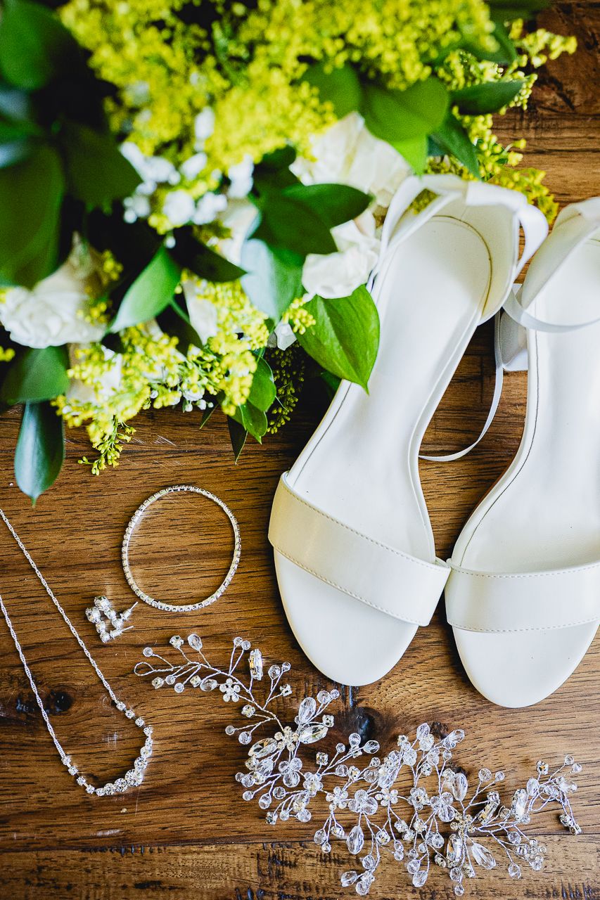 Wedding accessories flat lay with white sandals, jewelry and fresh green hydrangeas on wood.
