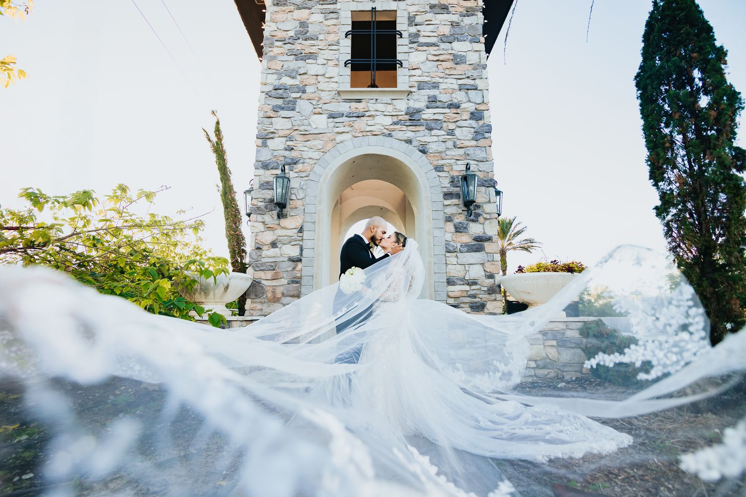 Dramatic wedding photo at stone chapel with flowing veil caught in the wind.