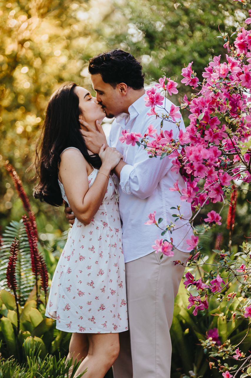 Romantic couple sharing a tender kiss in a garden with vibrant pink bougainvillea flowers in bloom.