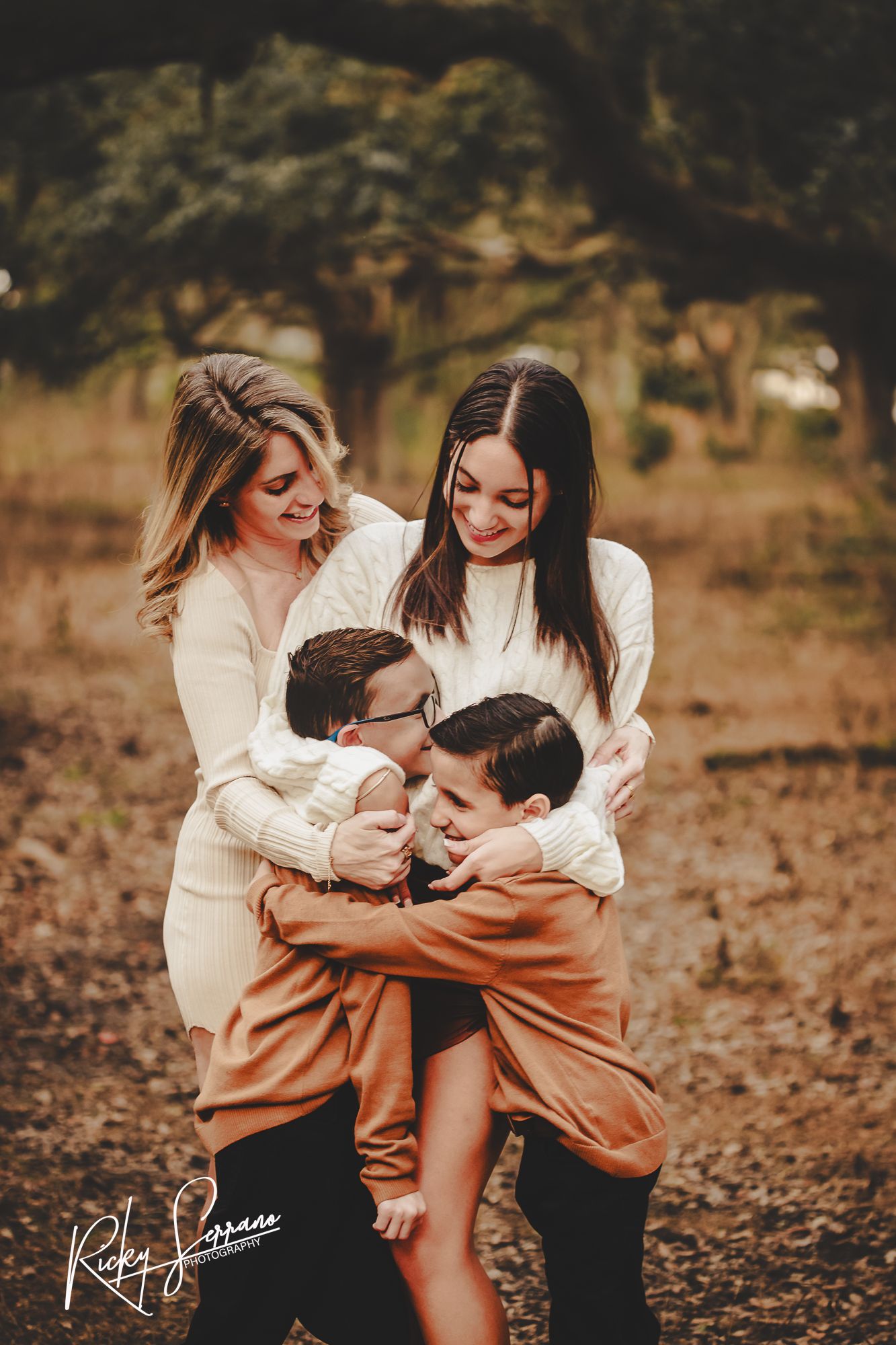 A family in white sweaters and brown pants sharing an intimate embrace outdoors during a fall photography session.