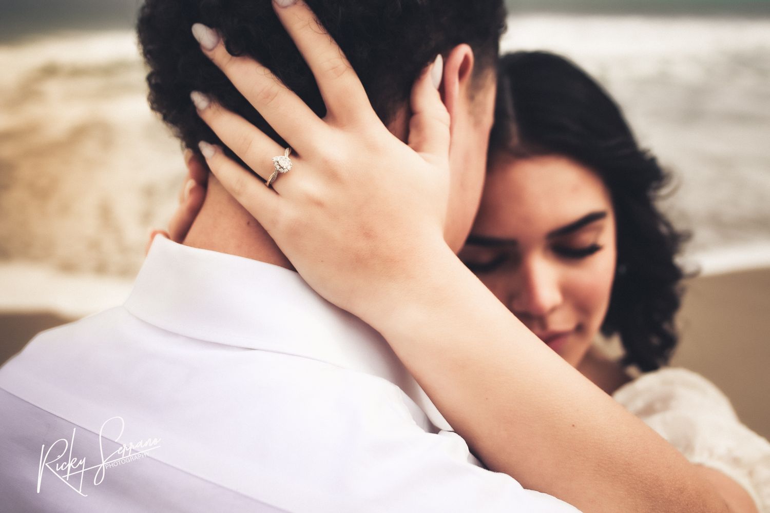 Close-up shot showing an engagement ring on hand embracing during an intimate romantic moment.
