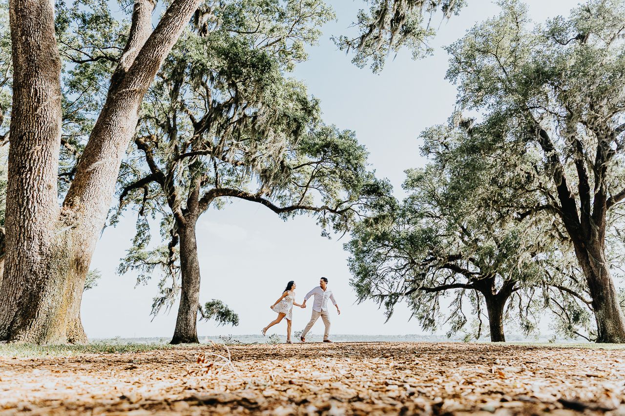 Silhouettes of a couple running through a pathway lined with majestic oak trees draped in Spanish moss.