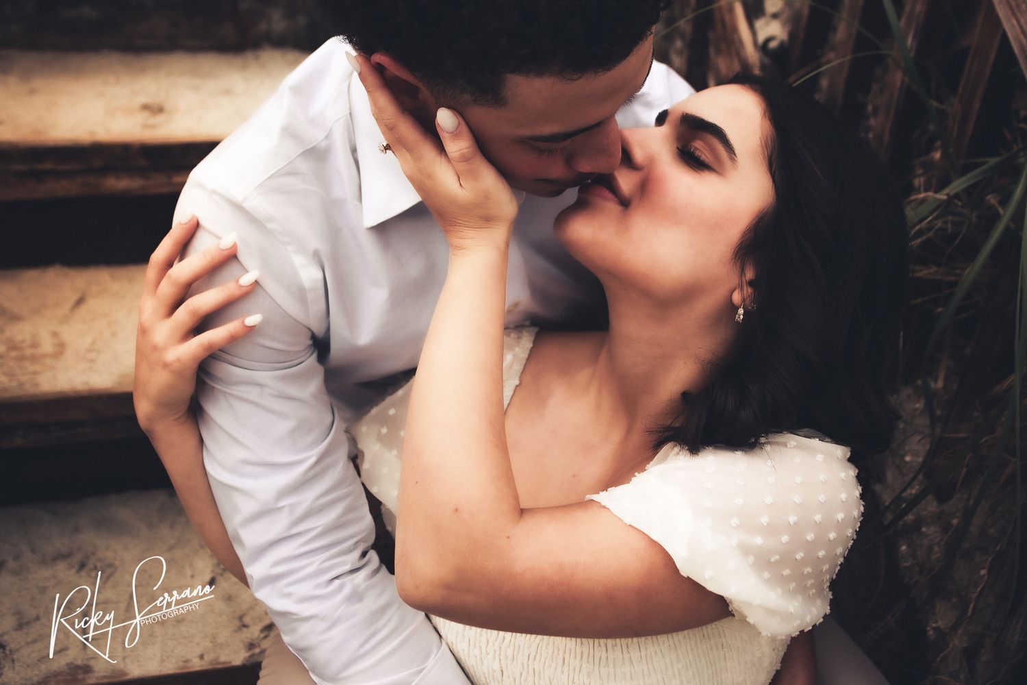 A romantic couple shares an intimate moment on rustic wooden stairs during their wedding photoshoot.