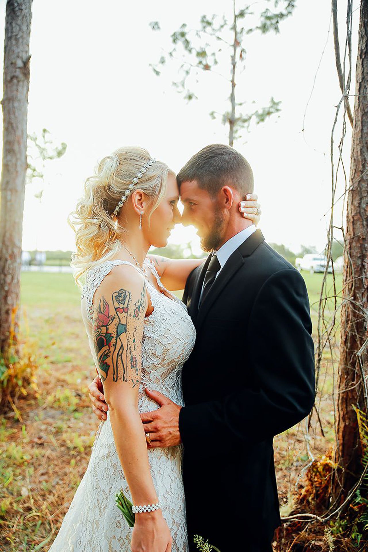 Romantic wedding portrait with lace dress and tattoo details in a natural outdoor setting.