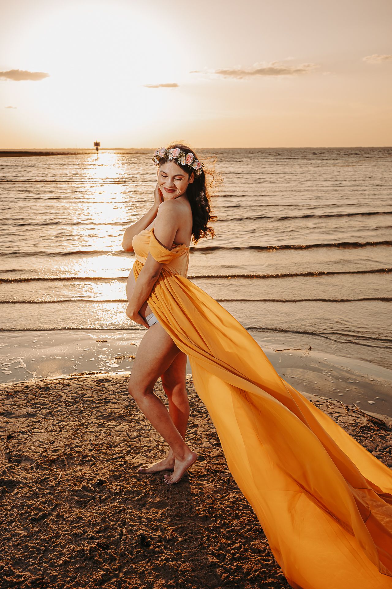 A flowing yellow dress billows in the ocean breeze during a golden sunset photoshoot on the beach.