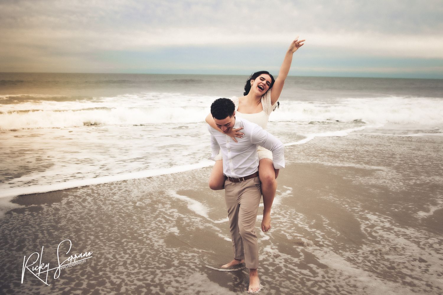A couple plays in the ocean waves during a beach photoshoot at dusk.