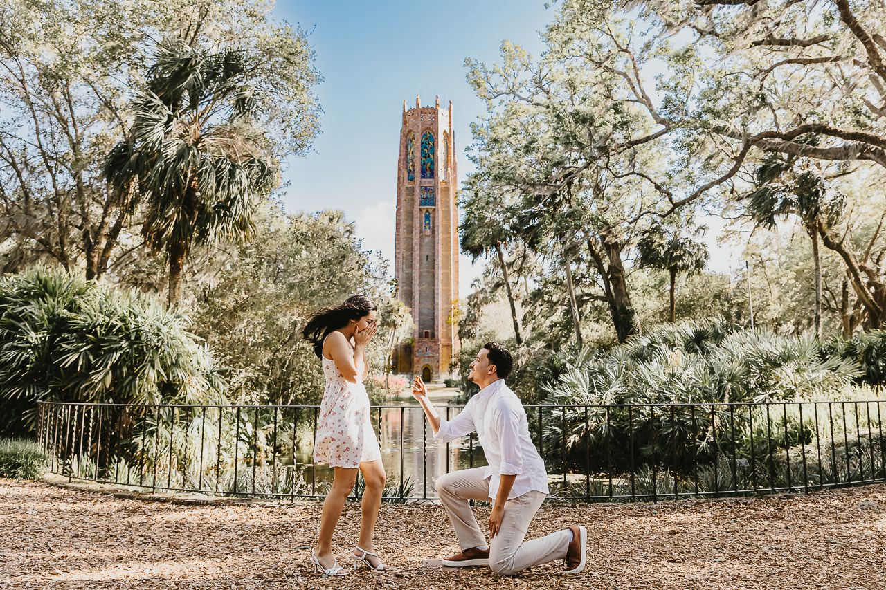 A romantic proposal scene in front of Century Tower at the University of Florida surrounded by blooming trees.