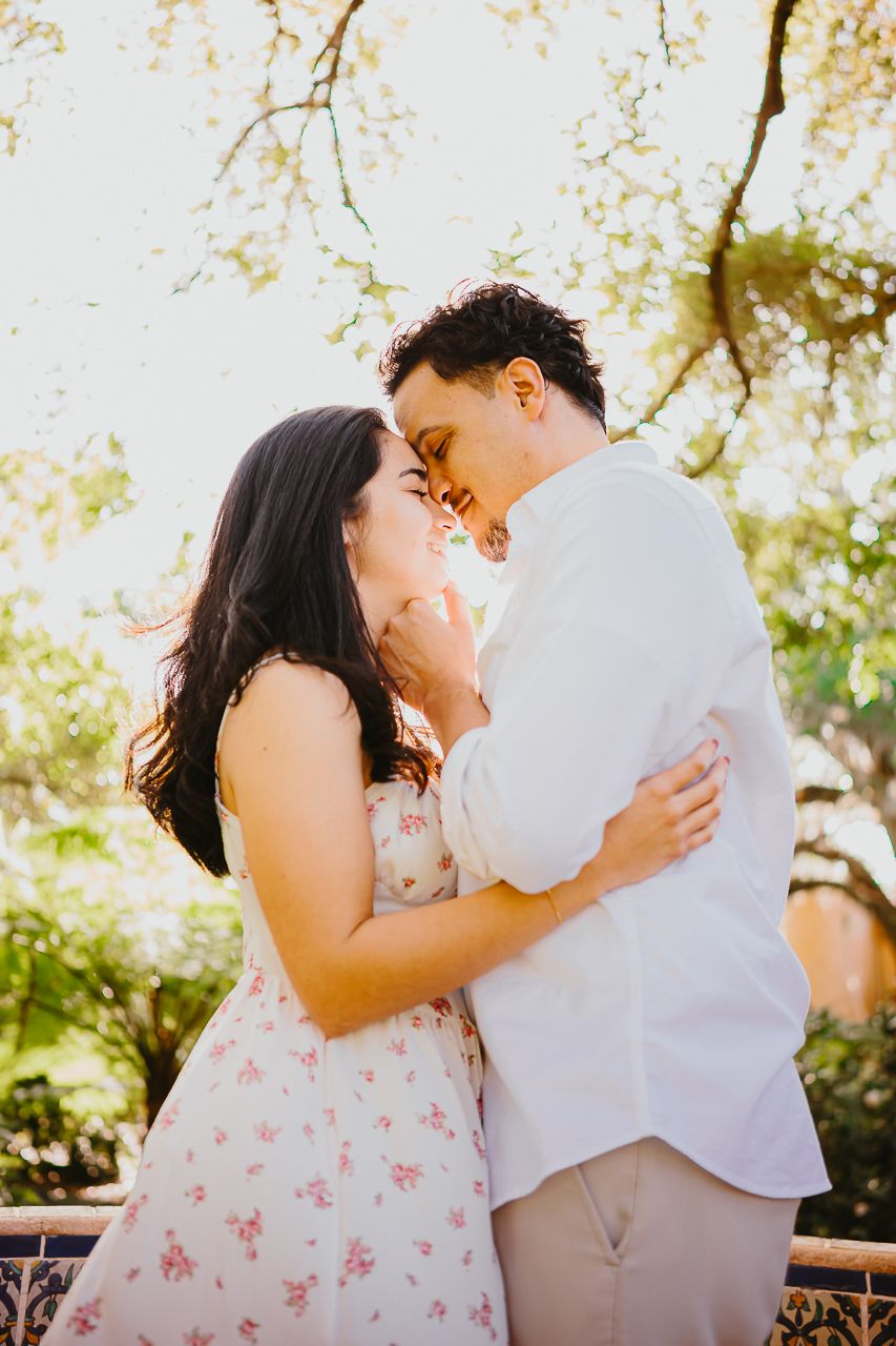 A couple shares a romantic moment outdoors while laughing and embracing in warm sunlight.