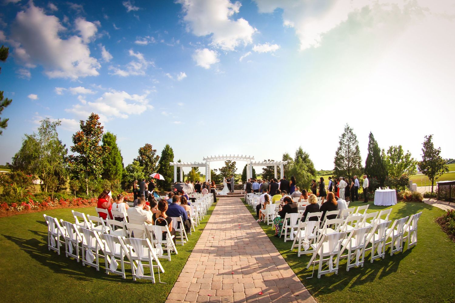 Outdoor wedding ceremony setup with white chairs and stone pathway under blue skies.