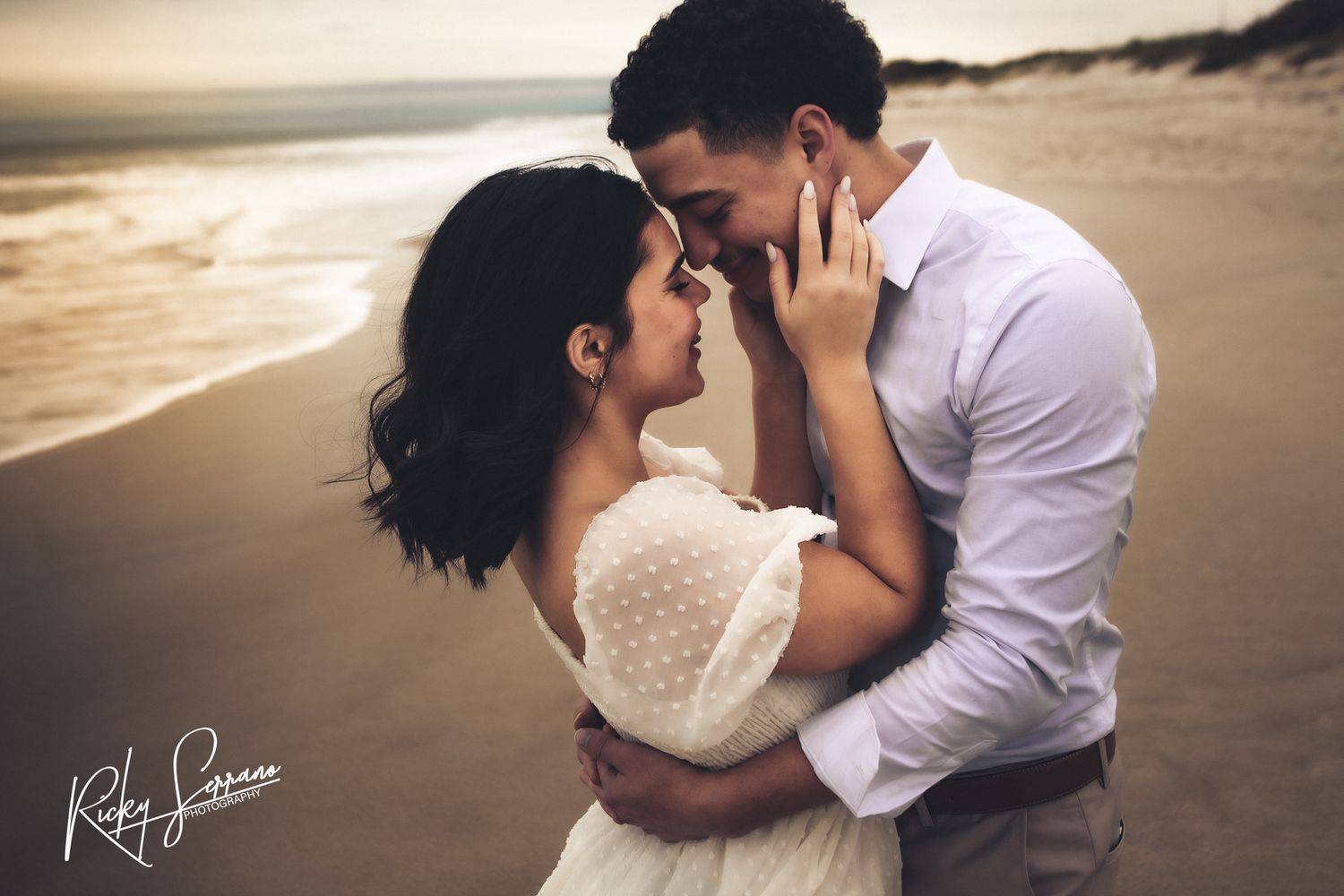 Romantic couple embraces on beach at sunset with waves crashing in background, creating intimate silhouette.