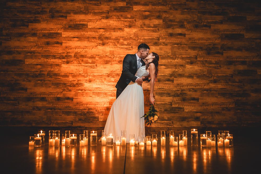 A romantic couple stands in silhouette against a brick wall surrounded by glowing candlelight on the floor.