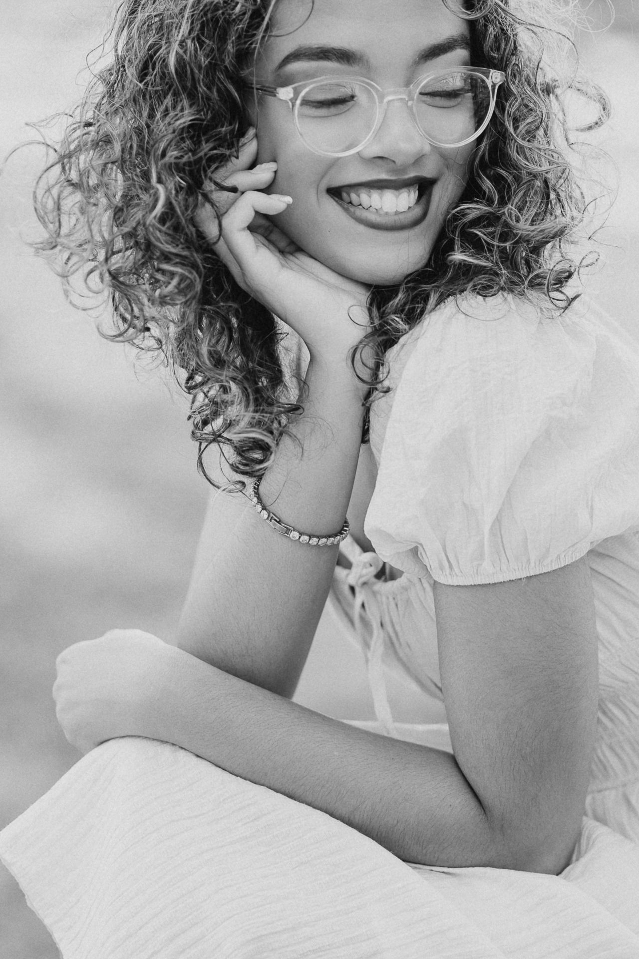 A black and white portrait of a woman with curly hair wearing glasses and a white dress.