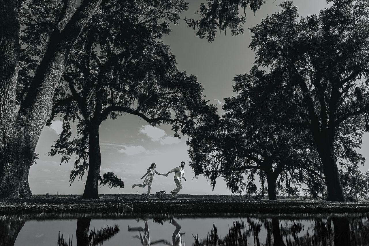 Two silhouettes dance on a waterfront dock with Spanish moss draped trees framing the scene in black and white.