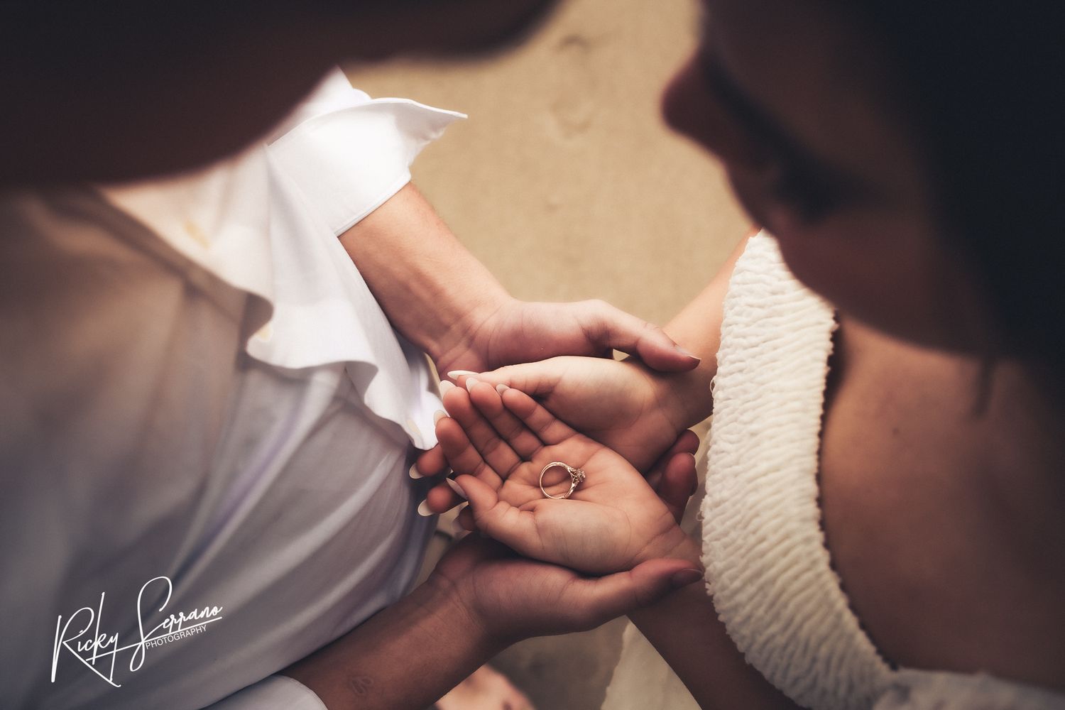 Two hands tenderly cupped together in an intimate moment during a wedding ceremony against white and beige tones.