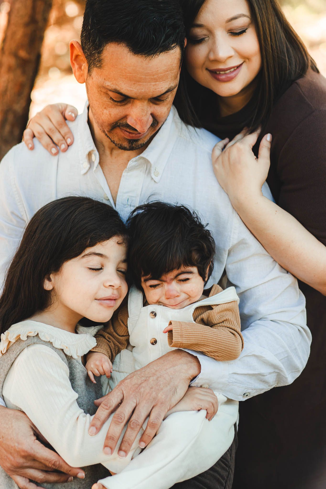 Close family moment captured outdoors with parents and two children snuggling together in warm sunlight.