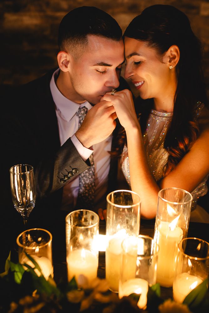 Romantic candlelit moment with couple in formal attire sharing an intimate gesture over glowing candles and champagne glasses.