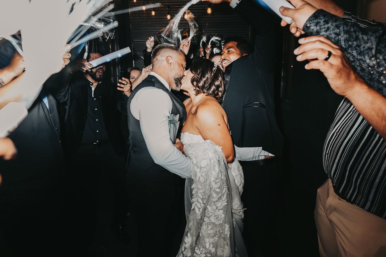 A couple shares an intimate moment on their wedding dance floor surrounded by guests with sparklers.