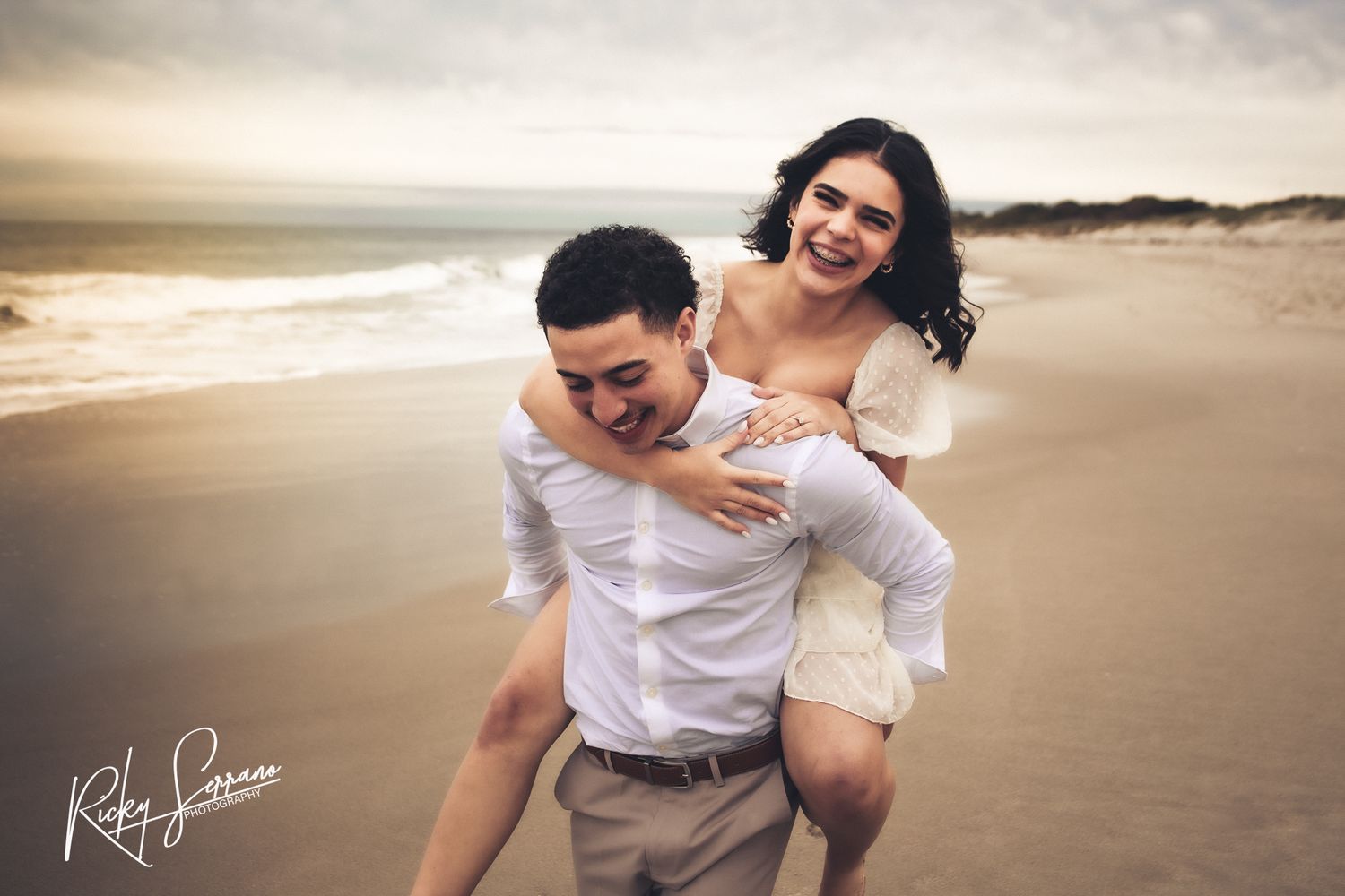 A couple shares a joyful moment together during a sunset photoshoot on a sandy beach.