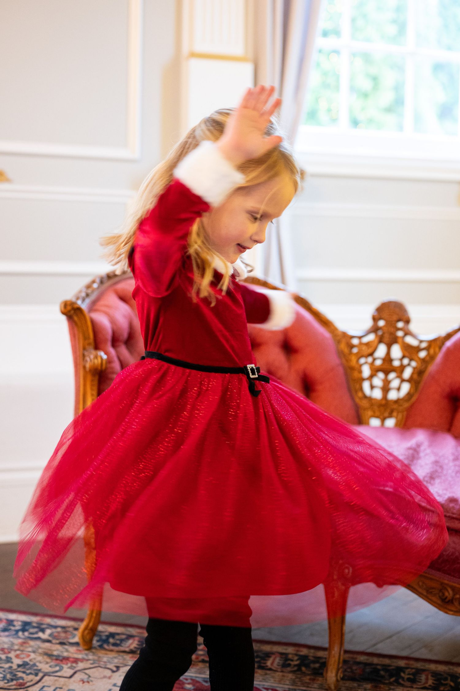 Young child twirling in red tulle holiday dress on patterned rug. Family session. Portrait photography. Oregon.