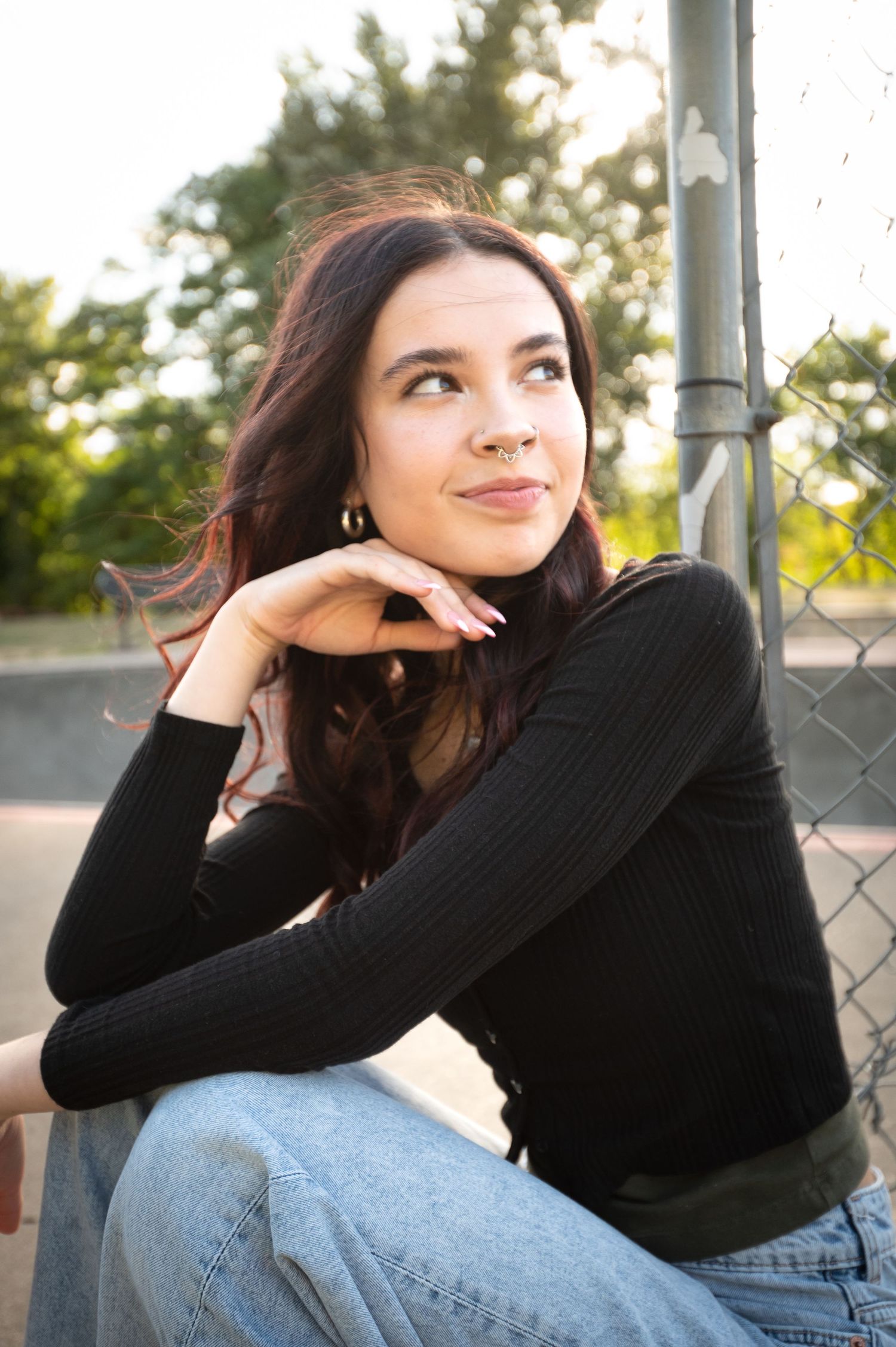 Portrait series in black sweater against chain link fence at sunset.
