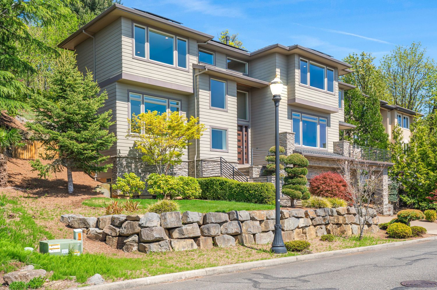 Modern hillside house with stone retaining wall and landscaping on sloped property. Real estate photography. PacWest Real Estate Media Group