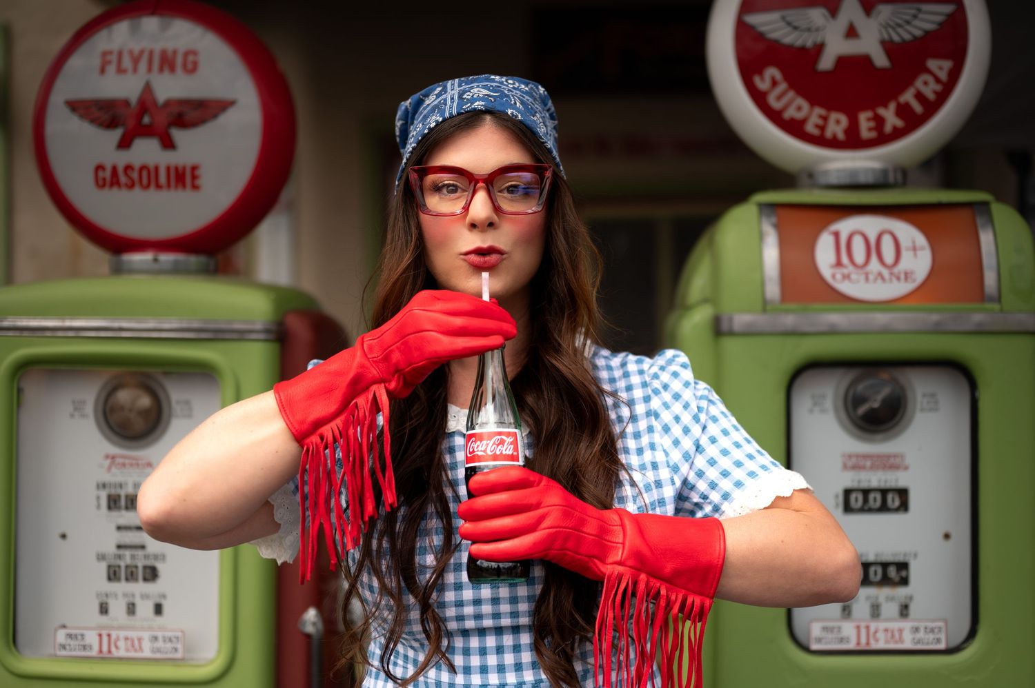 Vintage gas station signs and memorabilia displayed on wall with person wearing gingham dress and red accessories. Portland, Oregon.
