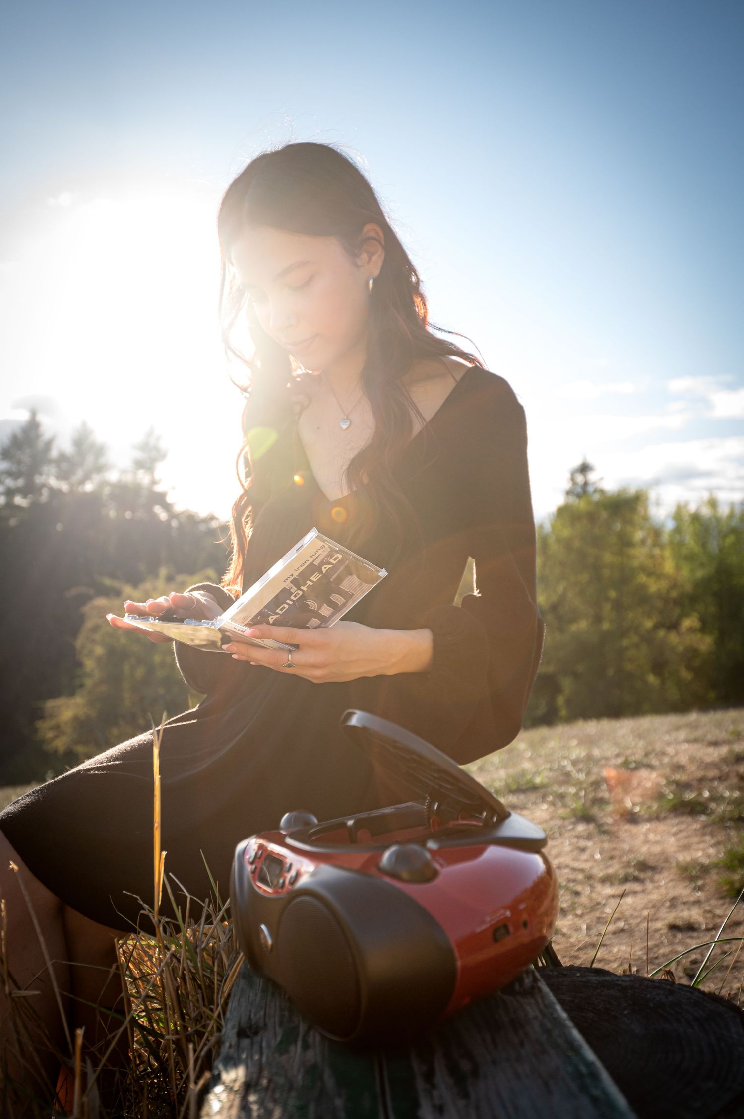 Person reading outdoors on rocky ground during golden hour sunset with lens flare.