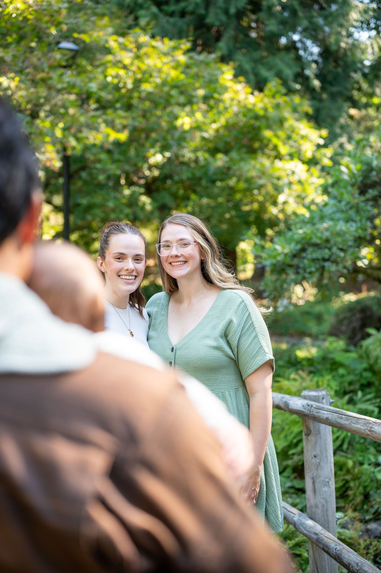 Couple sharing laughter while leaning on wooden fence in lush garden setting. Family session. Portrait photography. Oregon.