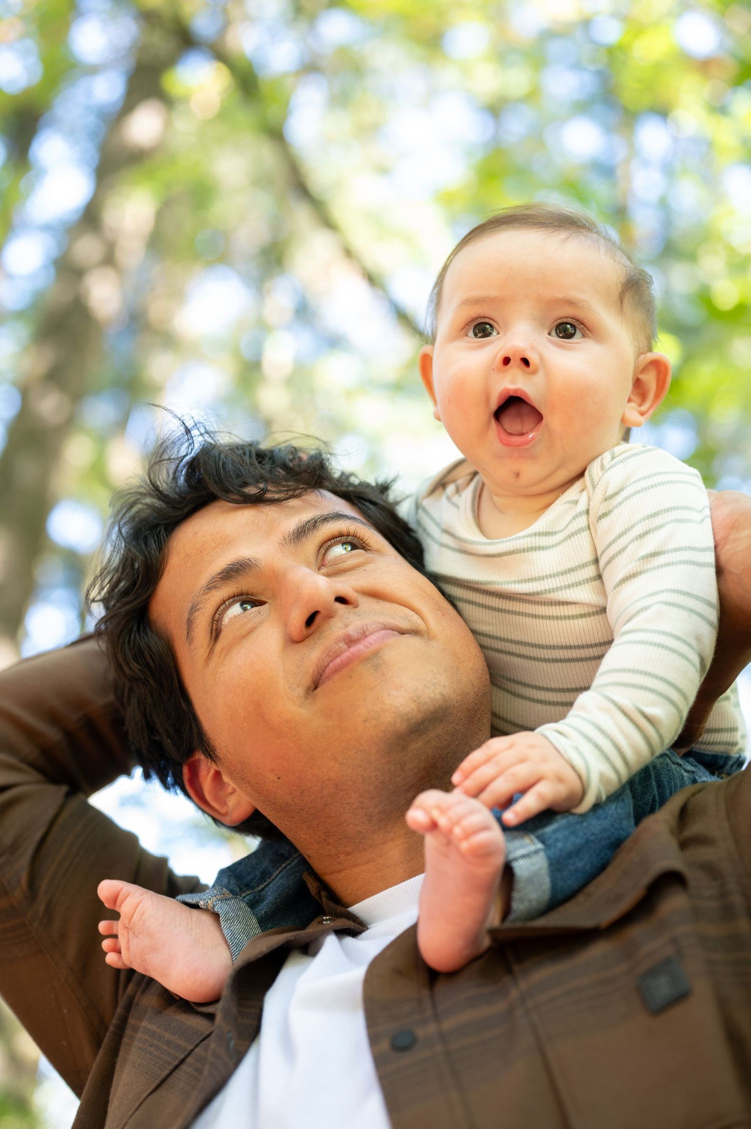 Playful interaction between parent and baby against sunny outdoor backdrop. Family session. Portrait photography. Oregon.