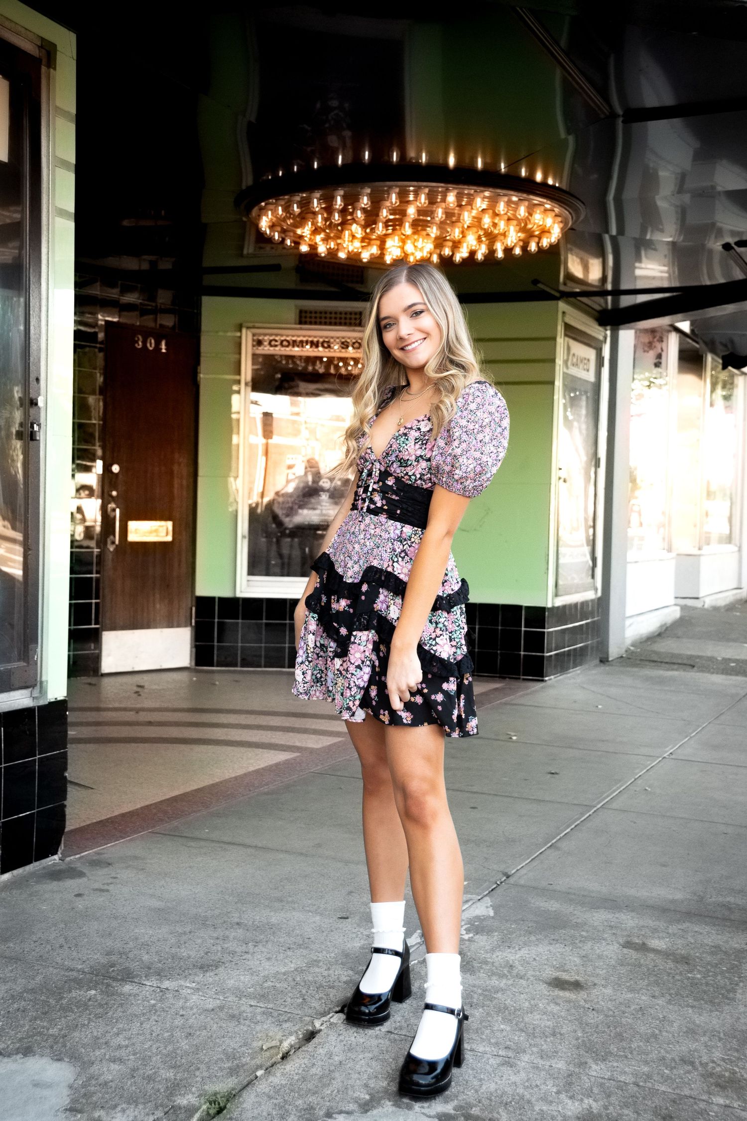 Person in floral dress and white socks poses playfully under ornate ceiling lights.