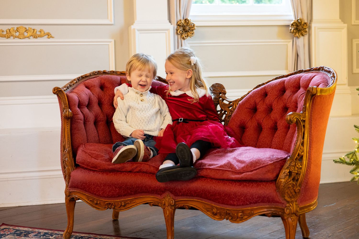 A burgundy vintage chaise lounge sits elegantly against a cream wall with ornate gold trim. Family session. Portrait photography. Oregon.