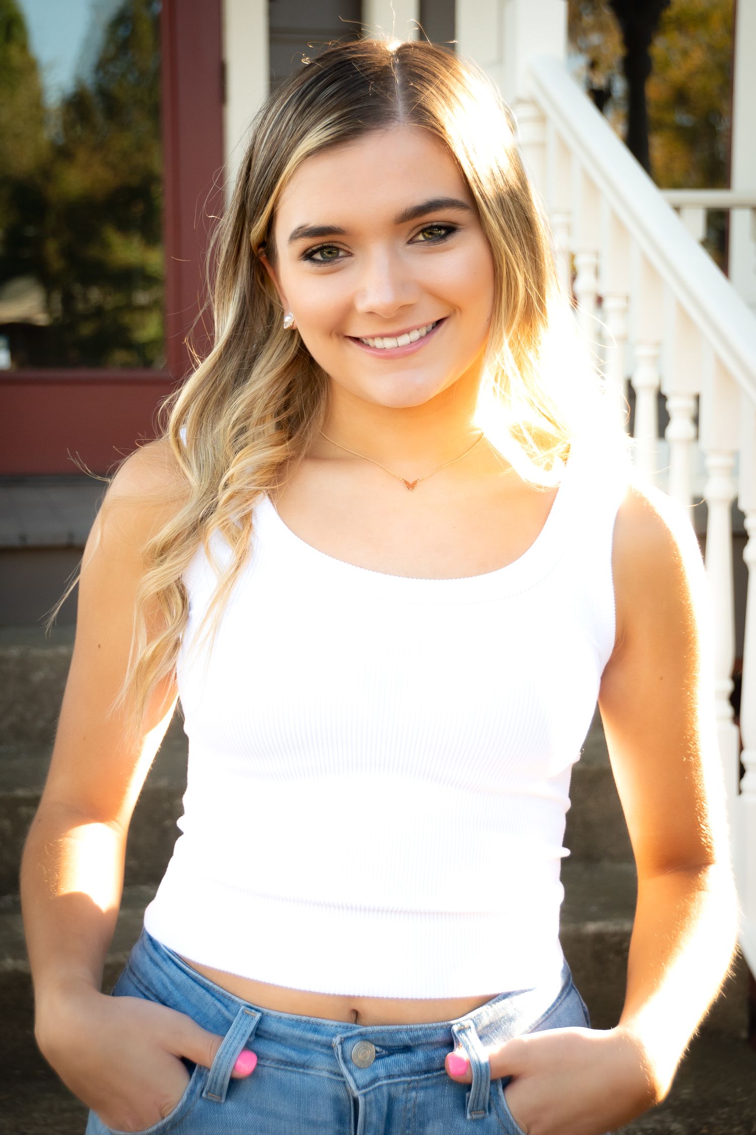 Sun-lit portraits in white crop top and jeans against white porch railing.