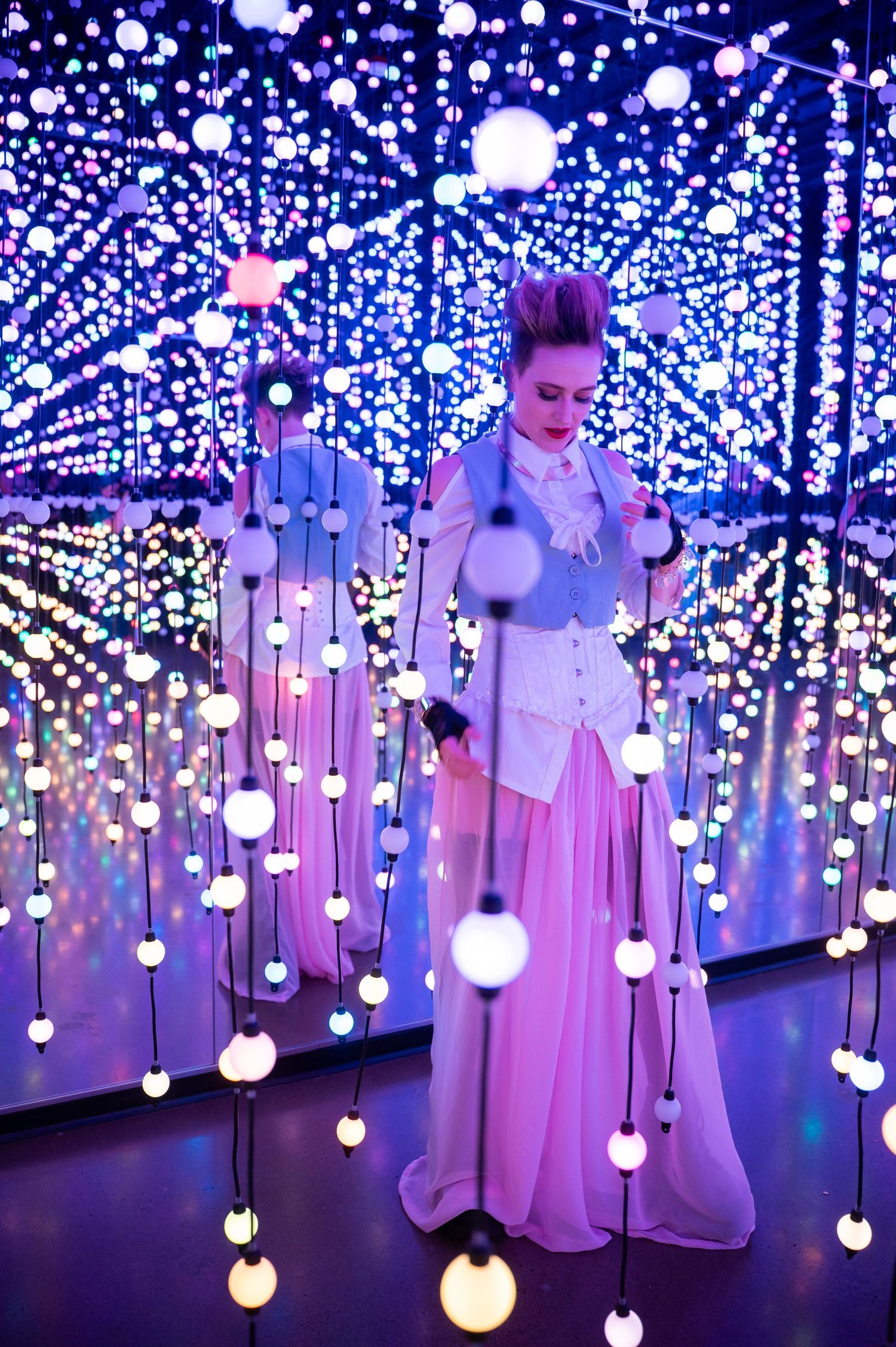 Elegant figure poses in flowing dress amidst hanging light installation. Hopscotch. Portrait Slam.