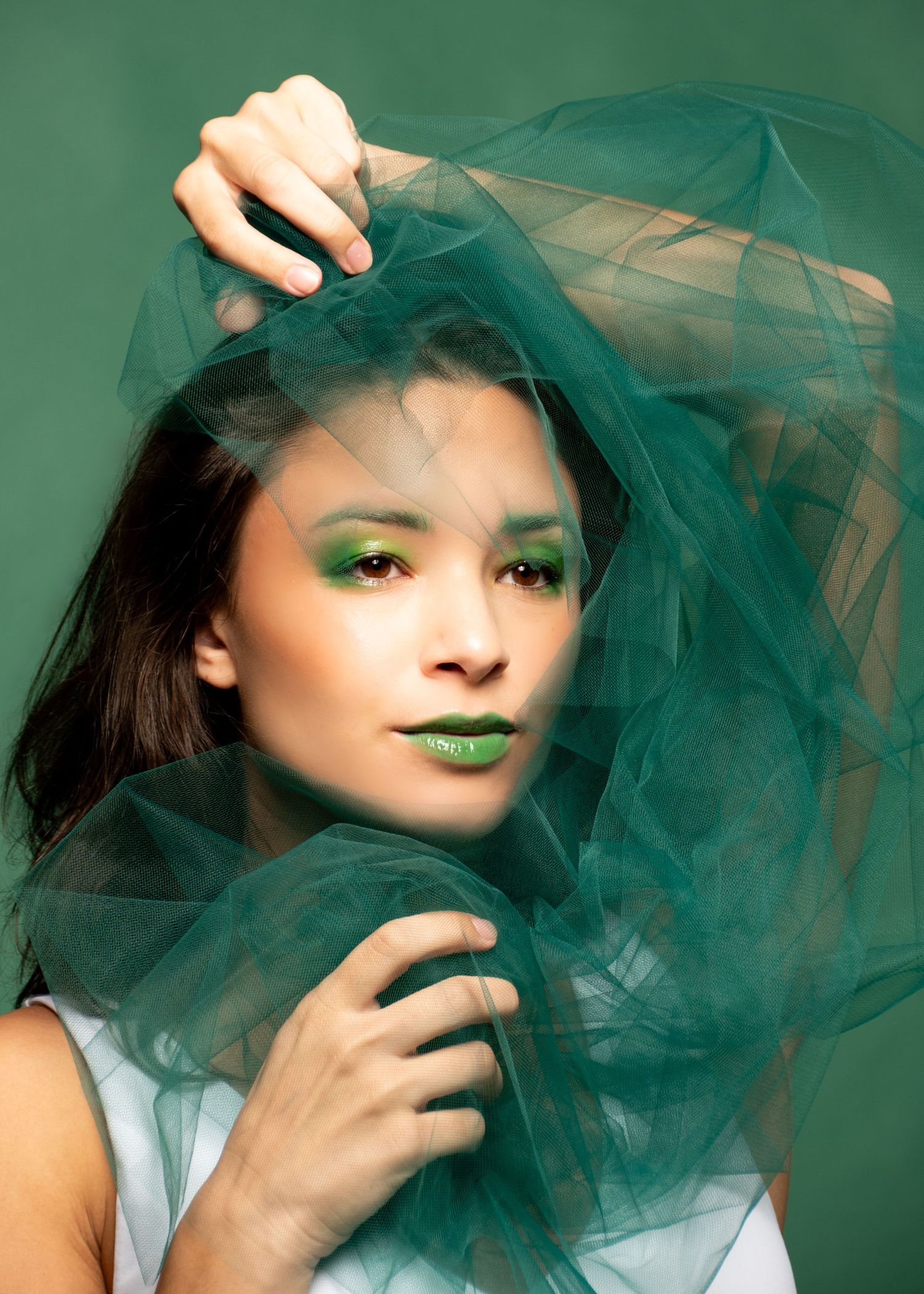 Creative portrait with teal tulle fabric against green background.