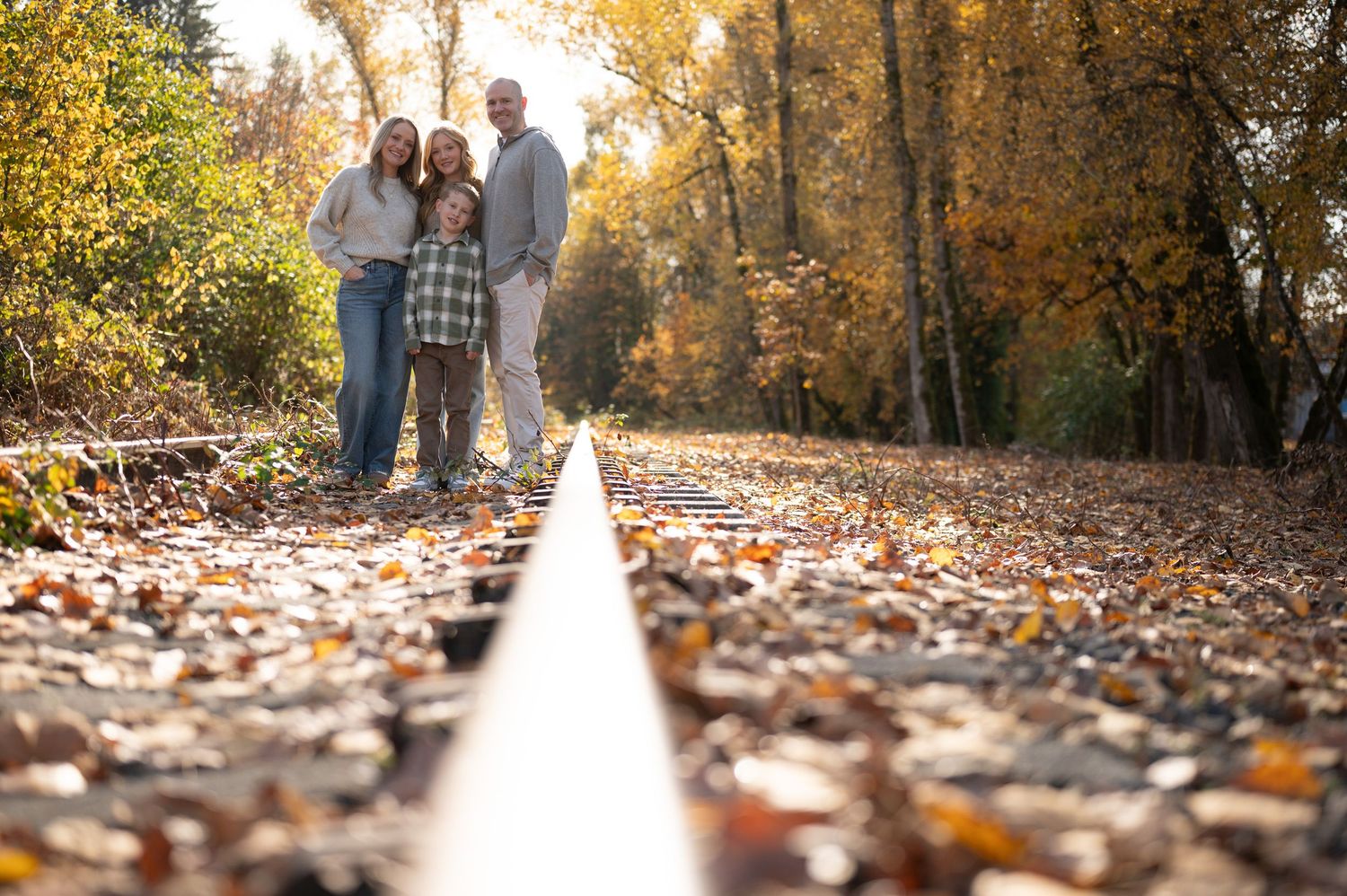 Low angle view of people standing on railroad tracks surrounded by fall foliage. Family session. Portrait photography. Oregon.