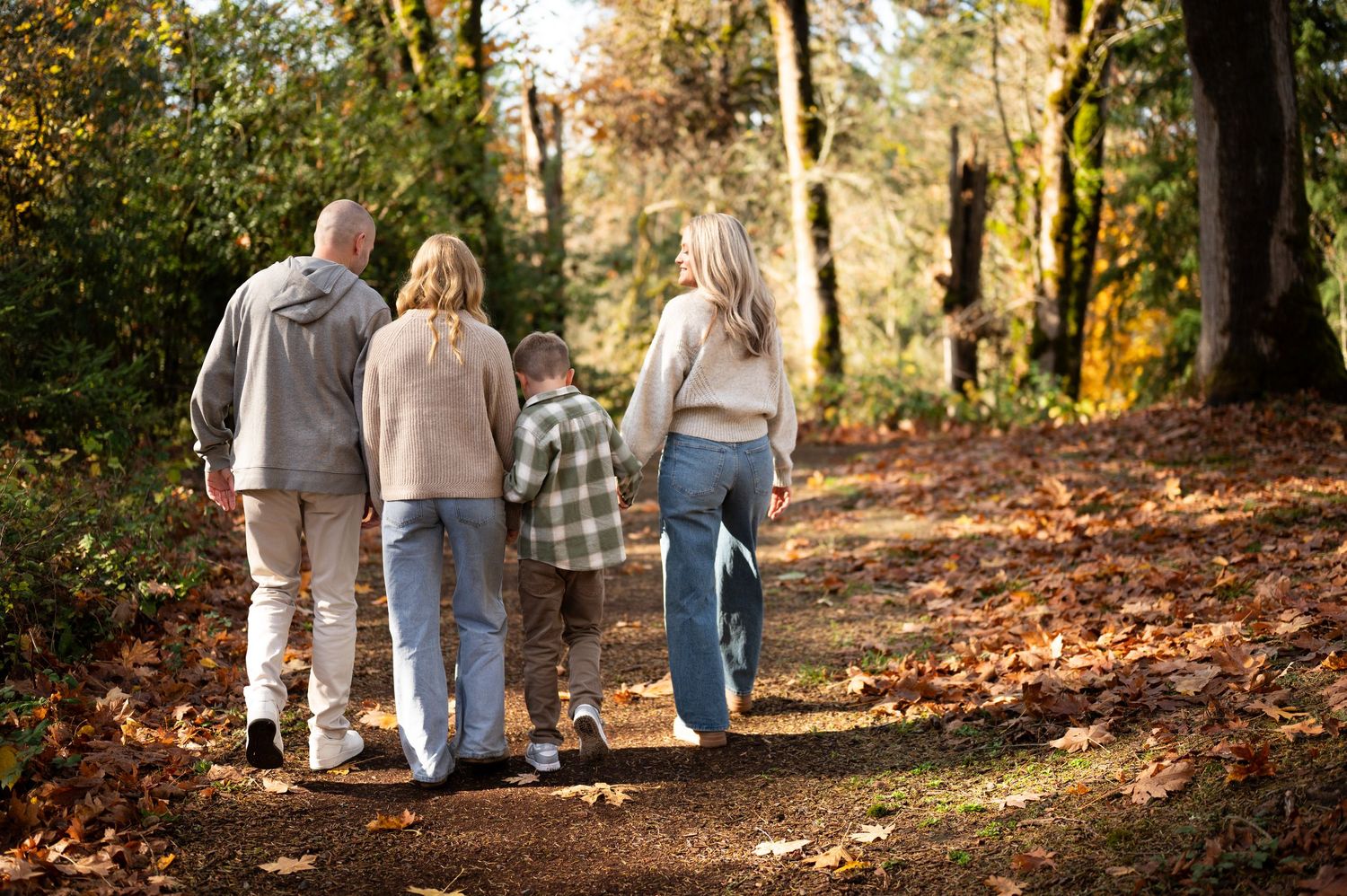 Group walking along a wooded trail covered in fallen autumn leaves. Family session. Portrait photography. Oregon.