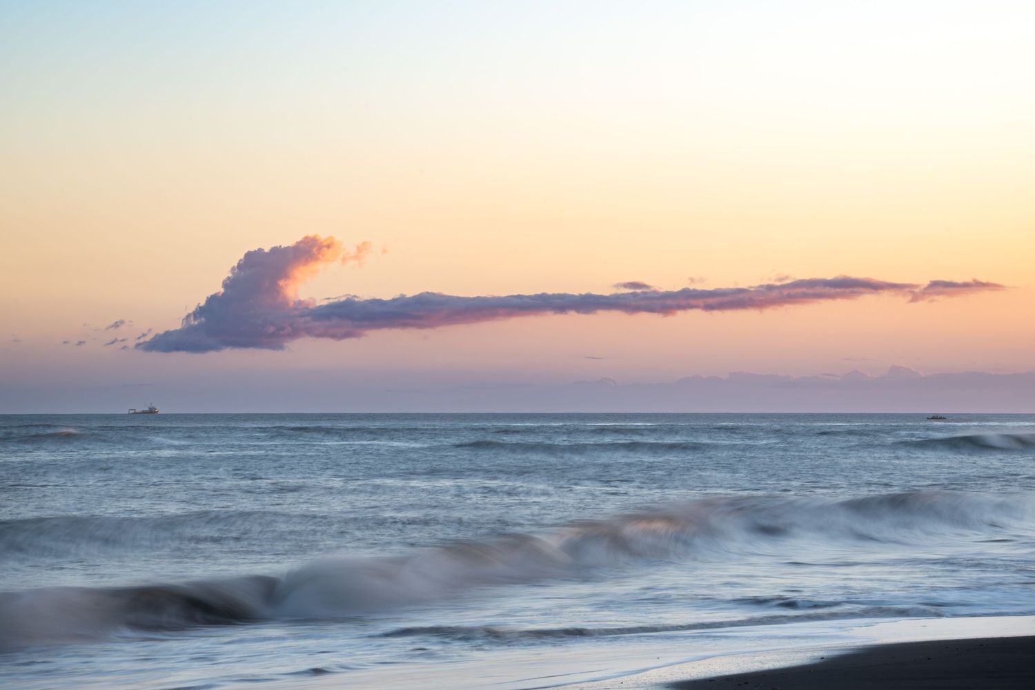 Serene ocean waves rolling onto shore during a pastel-colored sunset.