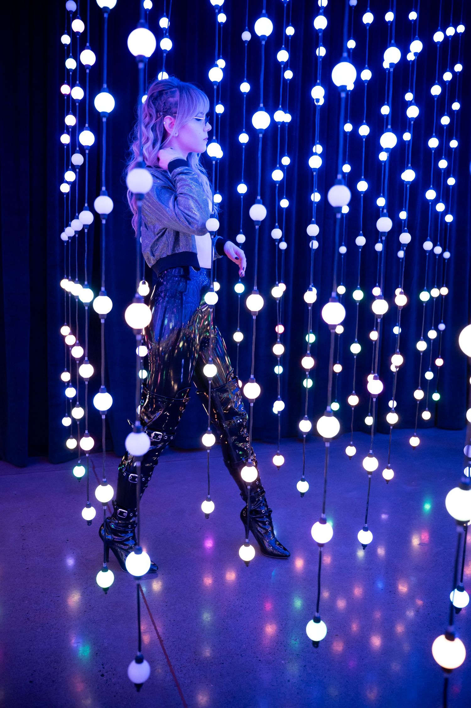 Figure poses dramatically among suspended glowing orbs in blue-lit installation. Hopscotch. Portrait Slam.