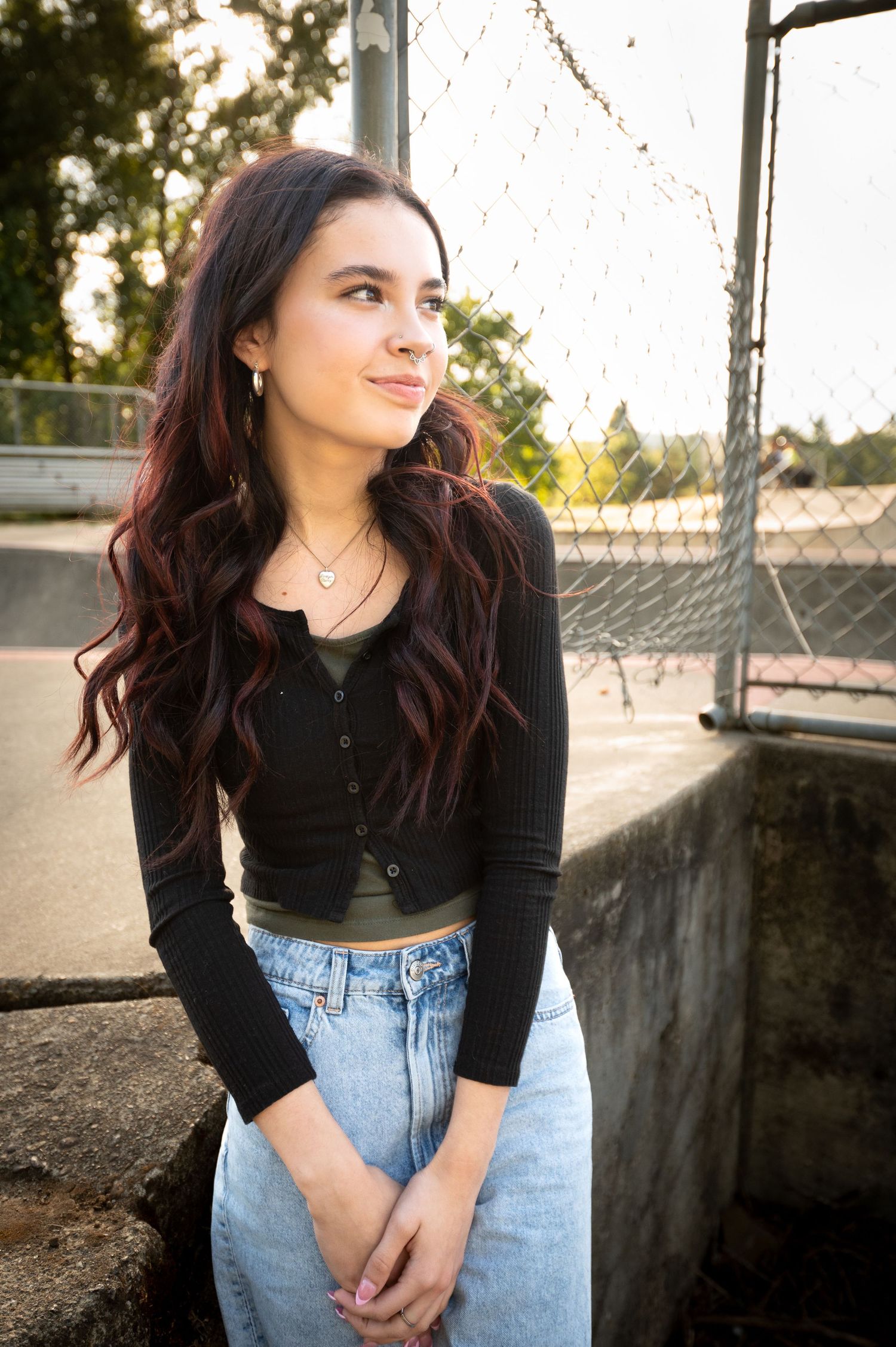 Casual outdoor portraits in black top and jeans near chain link fence.