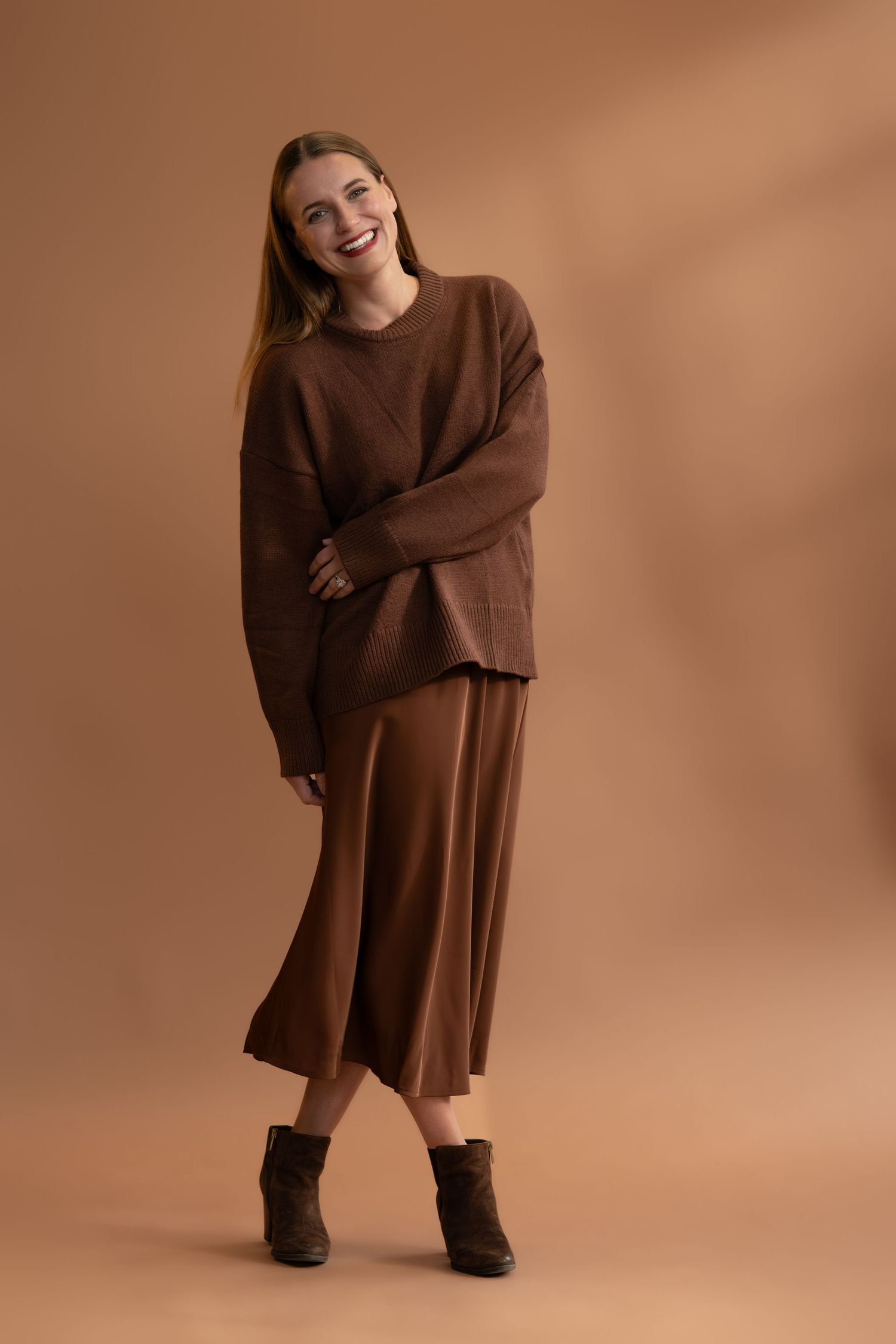 Fashion model in brown sweater dress showing playful movement in studio setting.
