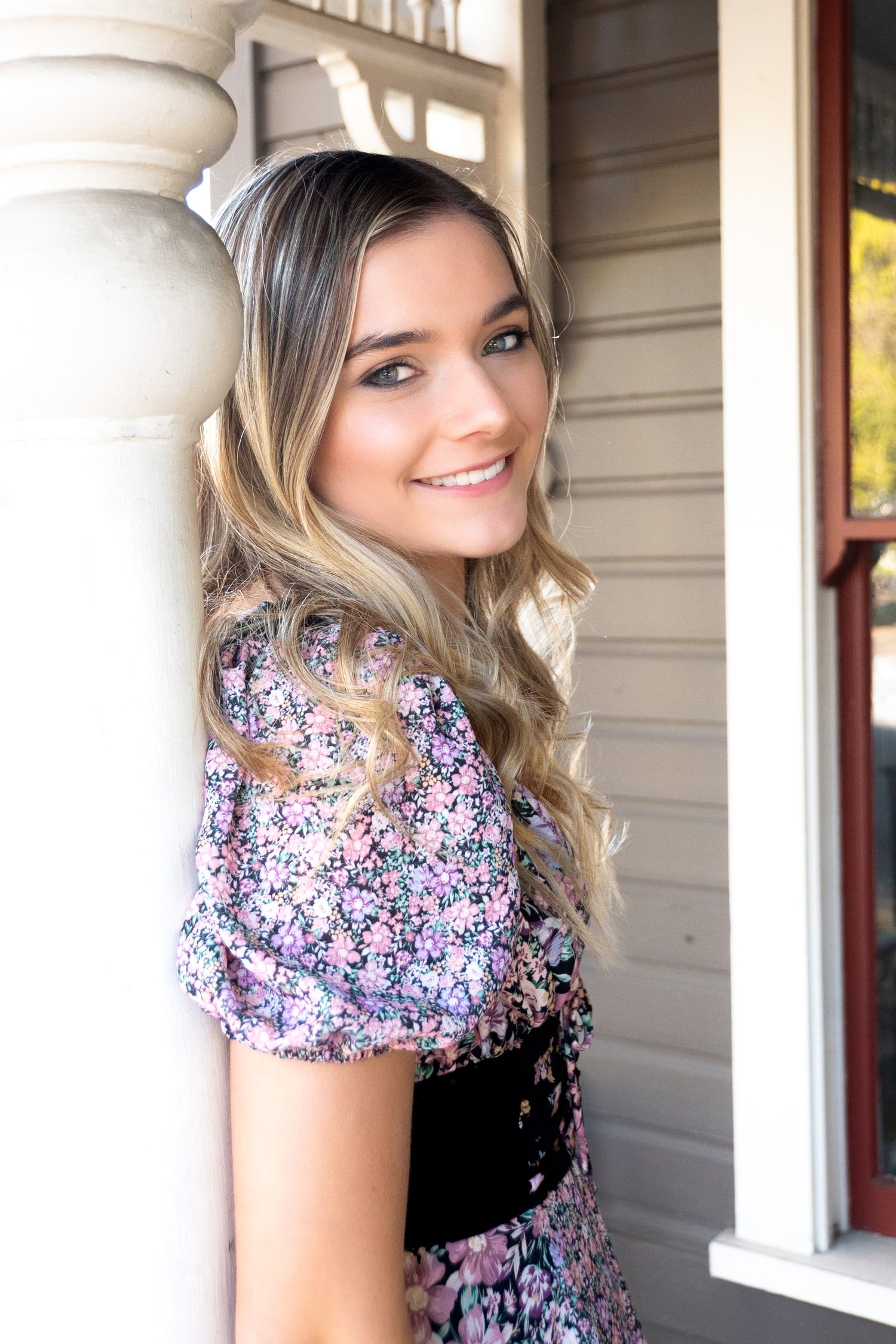 Portrait against white colonial style porch with floral dress and natural lighting. Senior photography. Newberg, Oregon.
