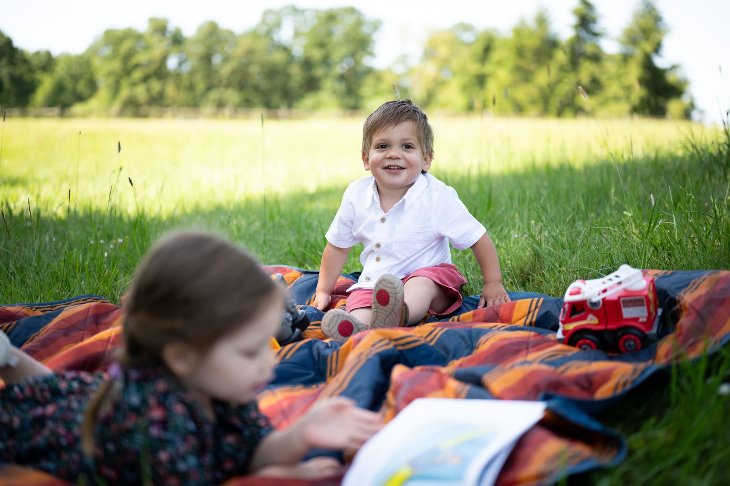 Children relaxing on blanket outdoors in sunny grassy field. Family session. Portrait photography. Oregon.