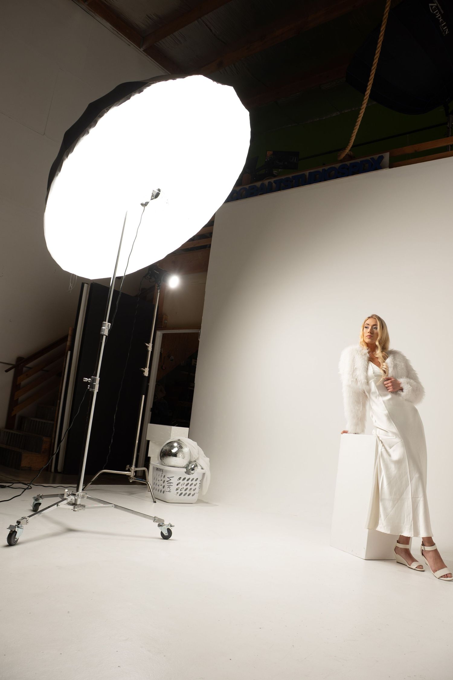 Behind the scenes photo shoot with lighting equipment and white backdrop in studio.