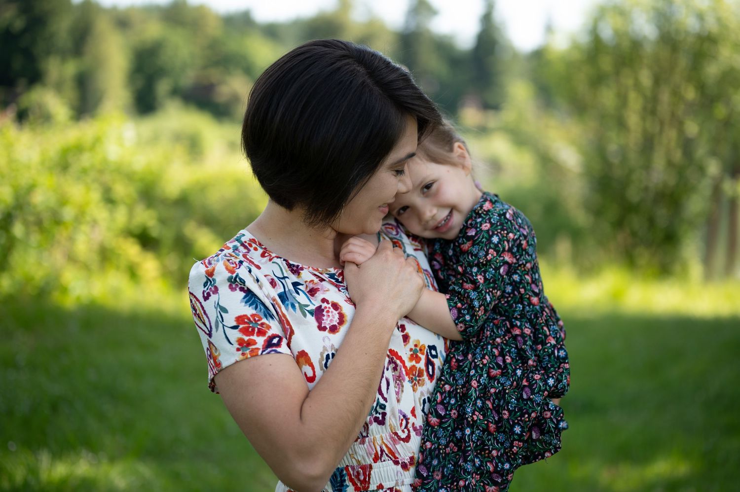 Two people embracing in sunny outdoor setting wearing floral print dresses.