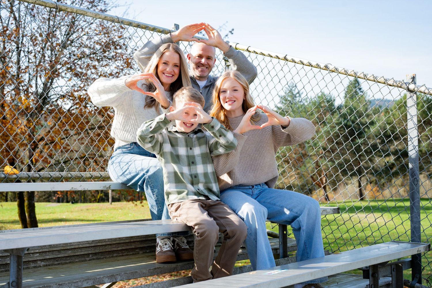Casual outdoor family photoshoot on a wooden bench near a chain-link fence. Go ducks! Family session portraits. Newberg, Oregon.