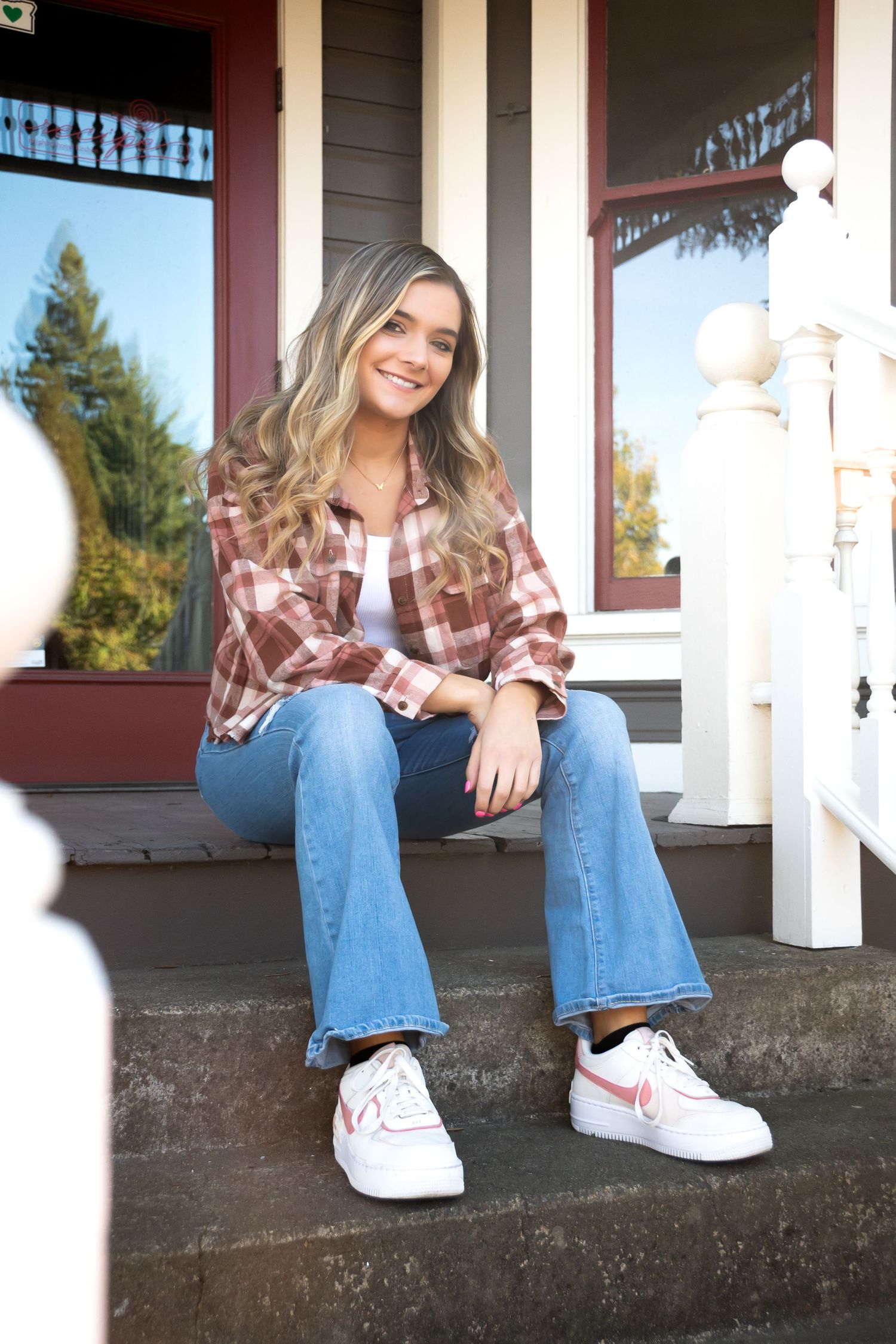Casual portraits sitting on porch steps wearing jeans and plaid shirt.
