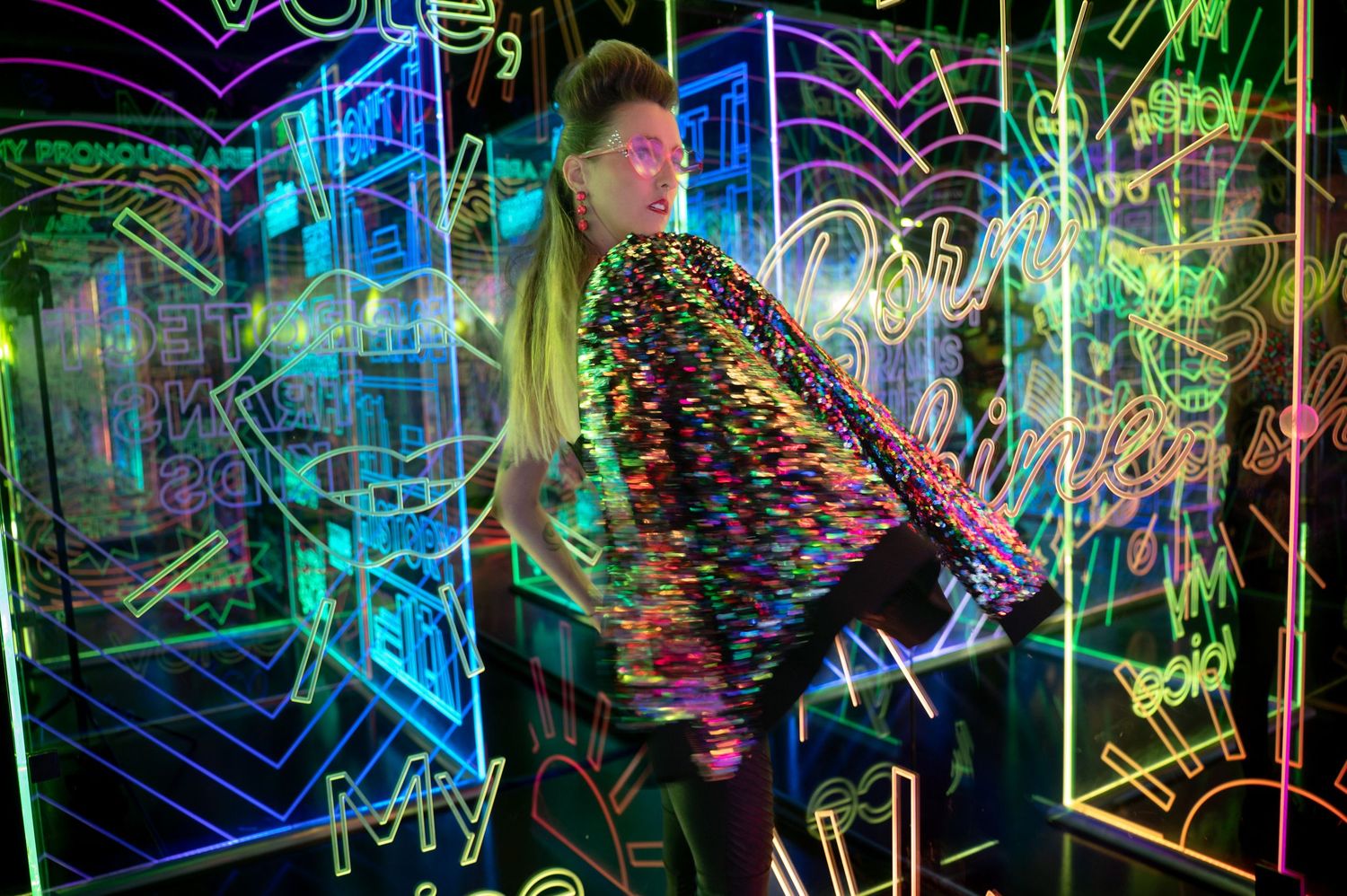 Performer in colorful attire dances amid neon geometric patterns and lights. Hopscotch. Portrait Slam.
