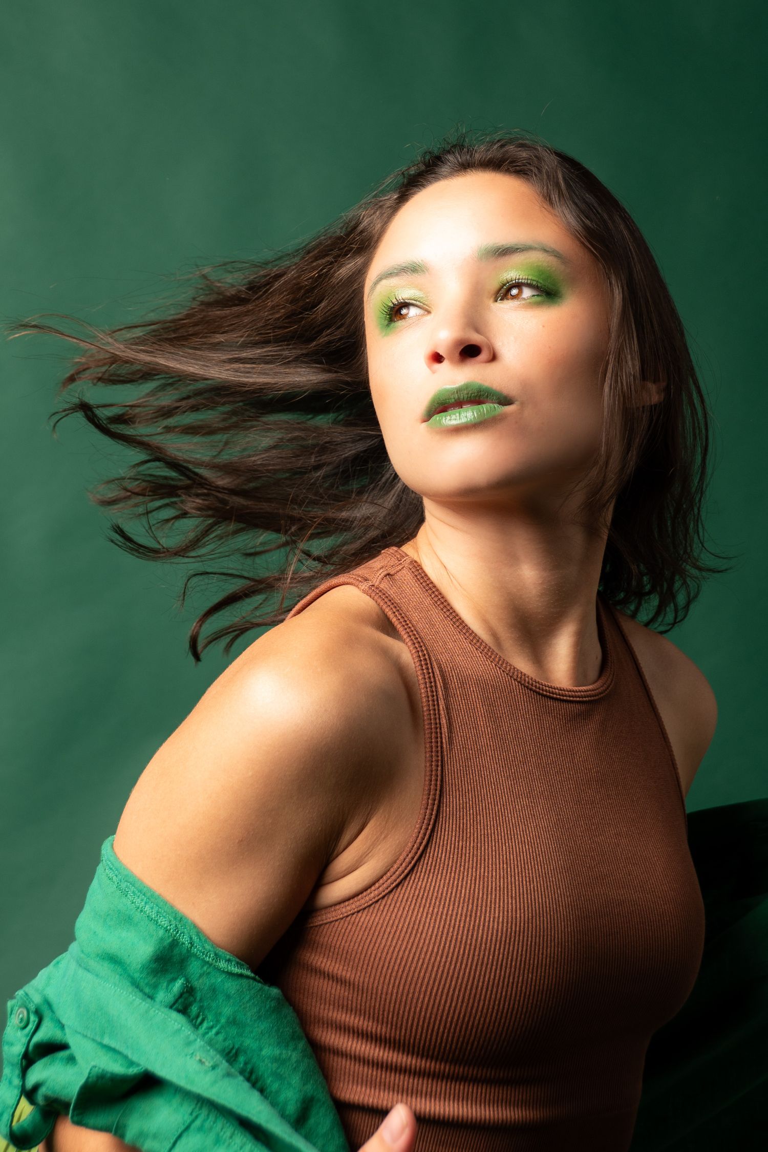 Fashion portrait in brown top and green styling against emerald background.